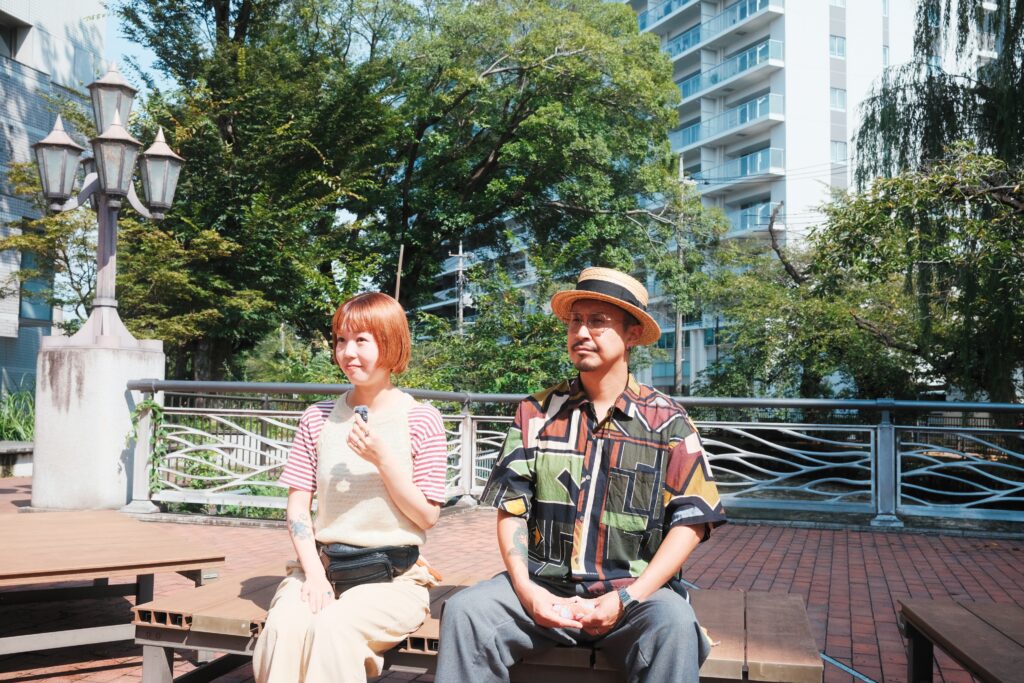 前橋の川沿いのベンチに並んで座る西澤康介さんと日菜子さん